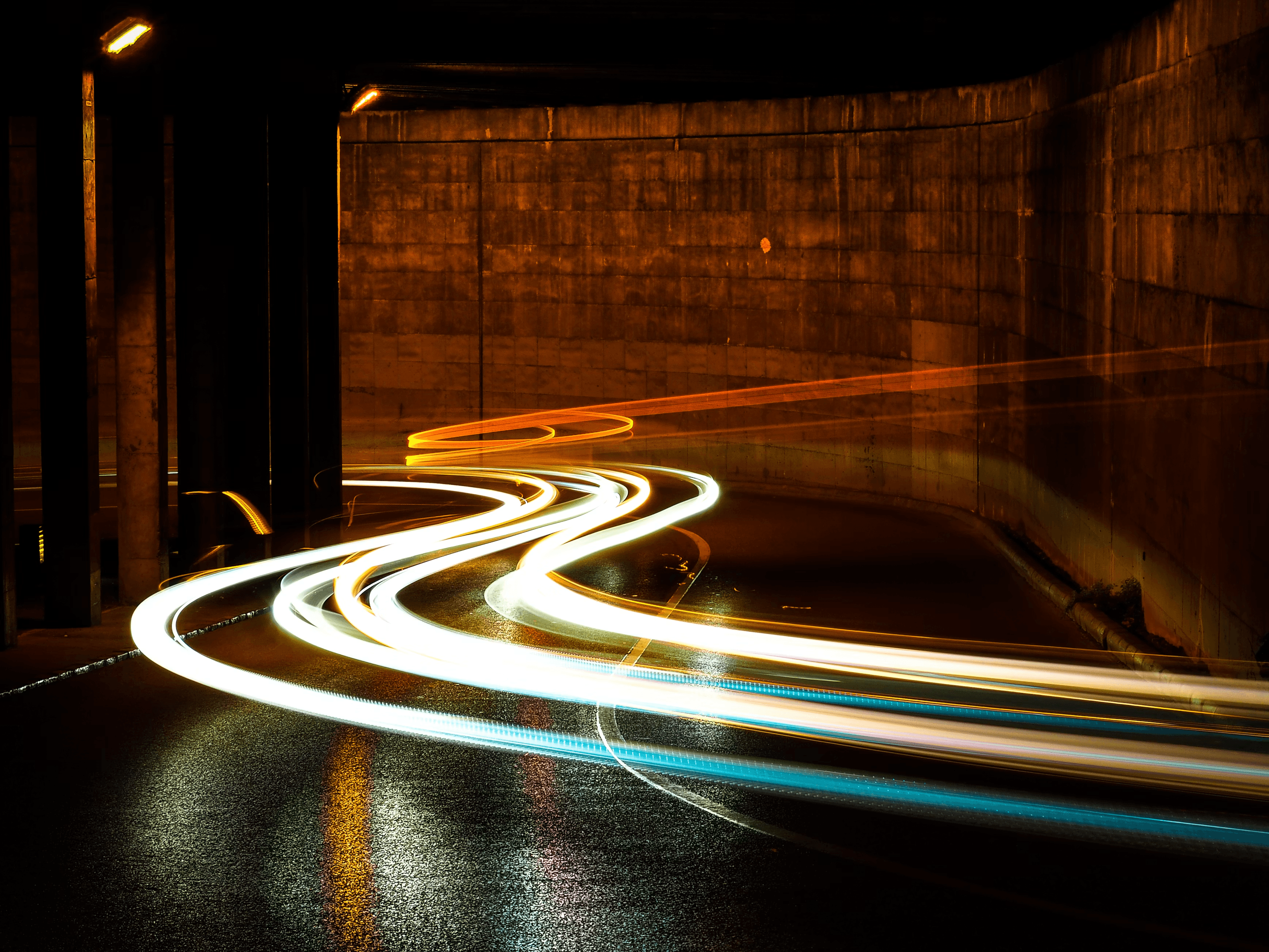 Long-exposure light trails from traffic curving through a road underpass at night